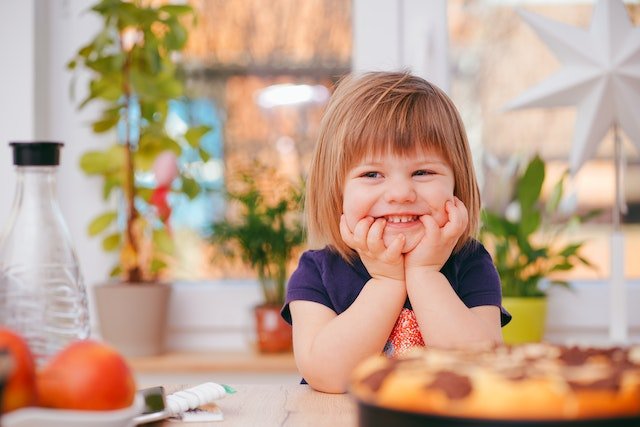 A young child holding their head in their hands and smiling very widely
