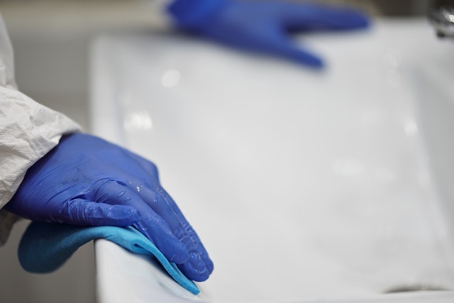 person with blue gloves wiping down white sink