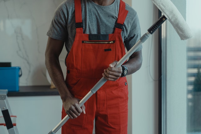 person in orange overalls holding window cleaner
