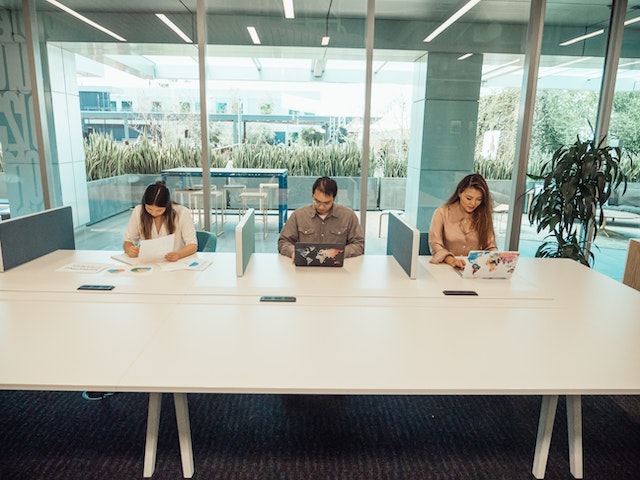 three people sitting at long desk in office