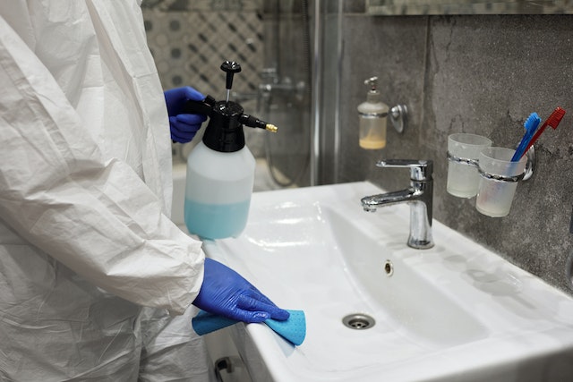 person in white oversuit and blue gloves cleaning bathroom sink
