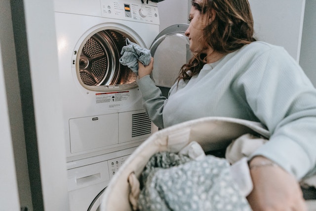 person holding a laundry basket loading laundry into a washing machine