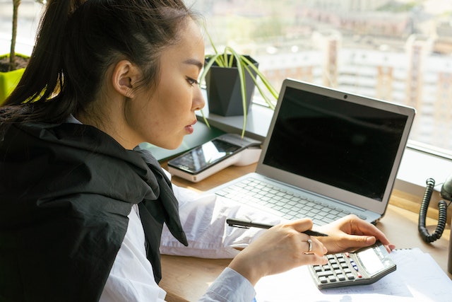 person on computer and using calculator on the side