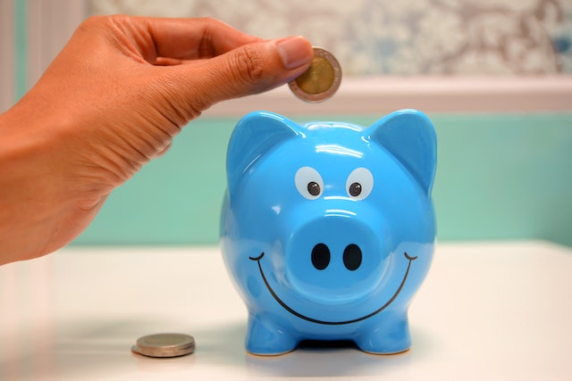 person dropping a coin into a blue piggy bank